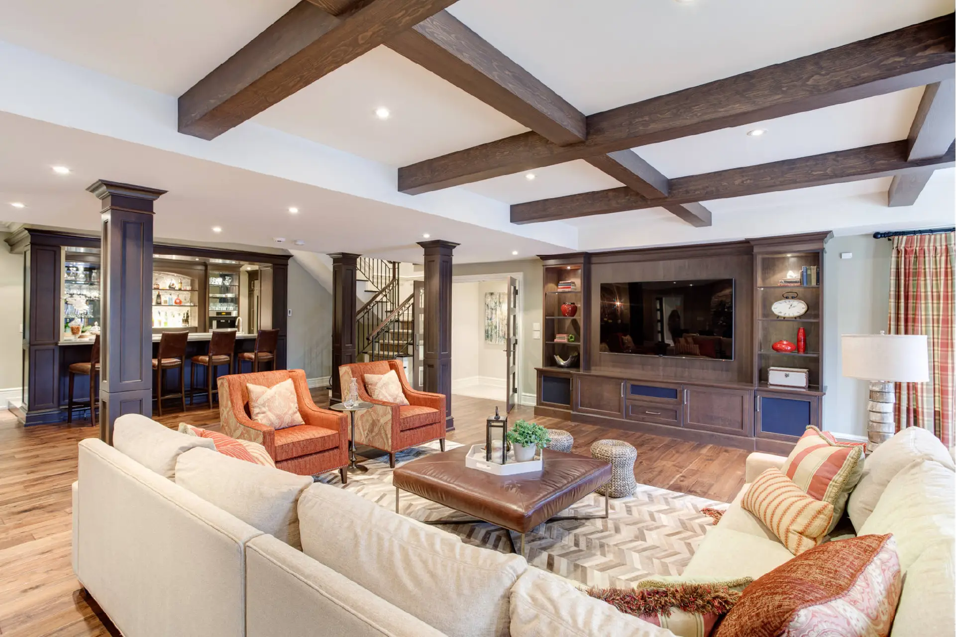 Luxury finished basement remodel in Fort Wayne by Home Enterprises Inc., featuring exposed wood ceiling beams, a cozy brick fireplace, and a spacious open-concept living area.