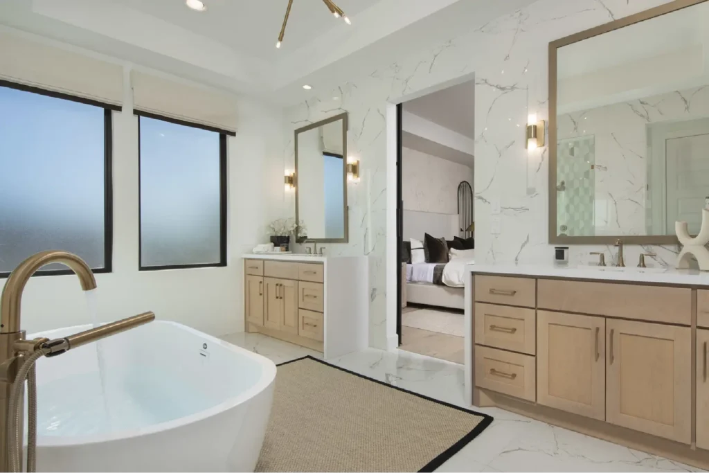 Fort Wayne Home Remodeling: Luxury bathroom remodel in Fort Wayne by Home Enterprises Inc., featuring a freestanding tub, light wood custom vanity, double sinks with elegant gold faucets, and stone floor tiles.