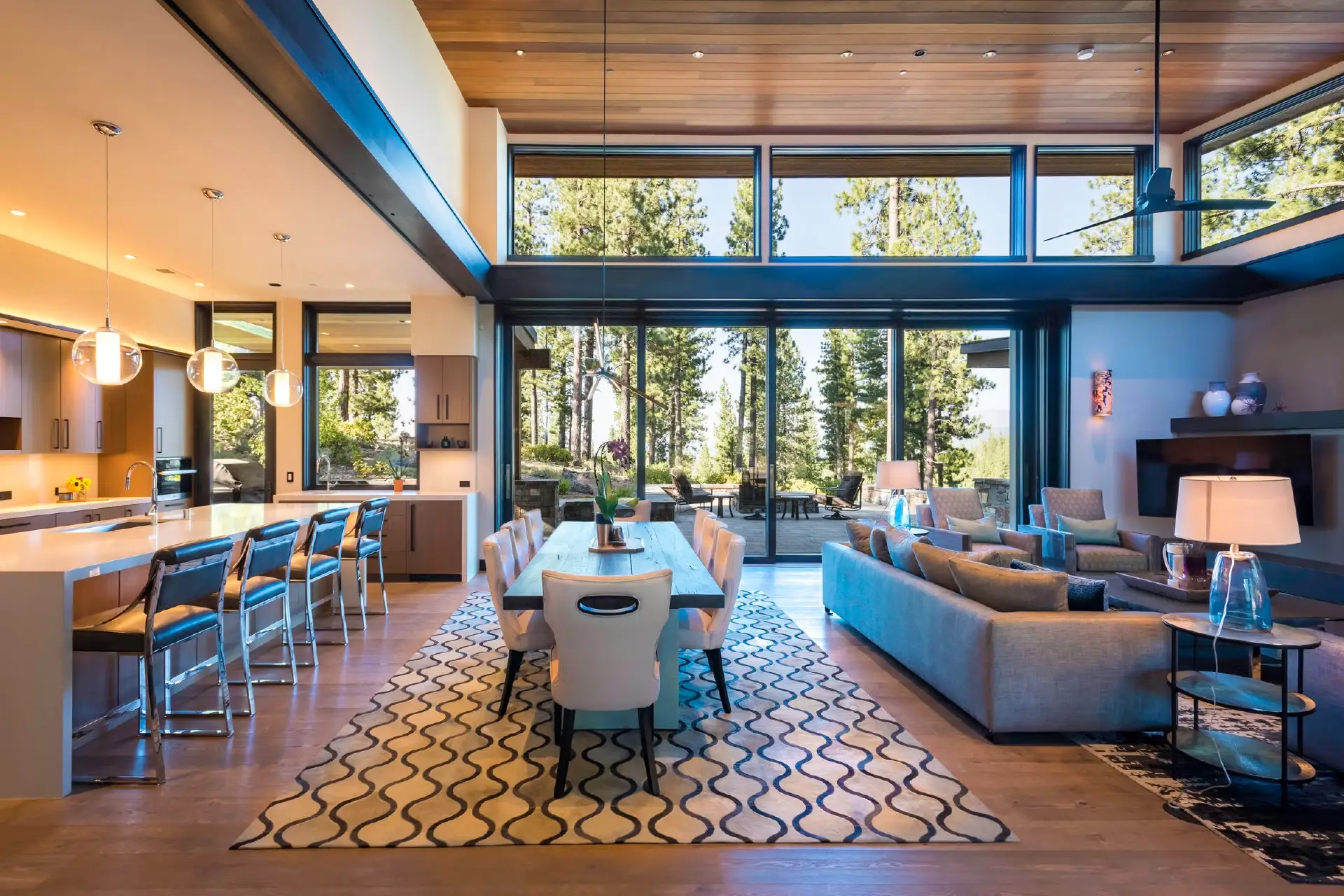 Modern open-concept living room remodel in Fort Wayne by Home Enterprises Inc., featuring a spacious sectional sofa, natural wood structural columns, and large windows looking out to a custom outdoor patio highlighting our luxury home remodeling services.