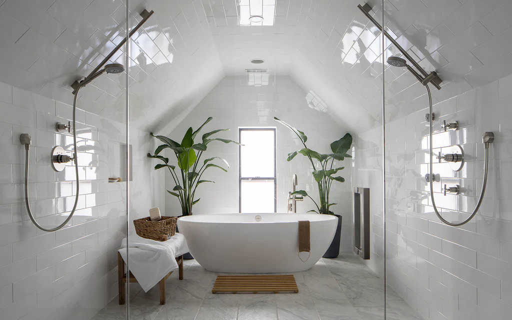 Modern white attic bathroom remodel in Fort Wayne by Home Enterprises Inc., featuring a freestanding tub, angled vaulted ceilings, a central window, and minimalist green plants.