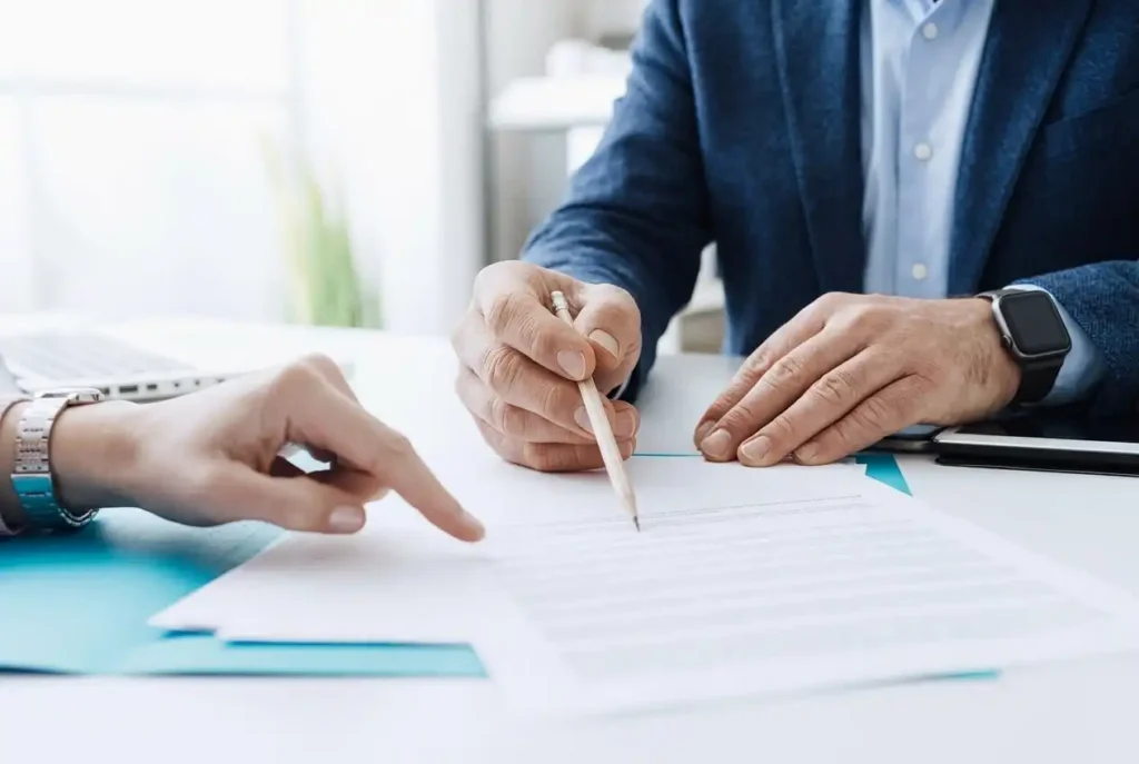 A close-up of a contractor pointing to a detailed remodeling proposal document while reviewing it with a client.